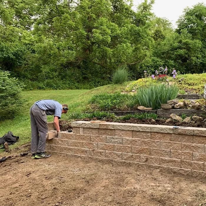 A crew member setting blocks on a long retaining wall at the foot of a sloped yard