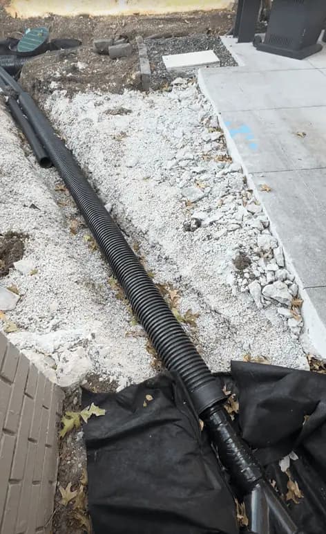 Black drain pipe laid in white gravel alongside a concrete walk, ready for new concrete