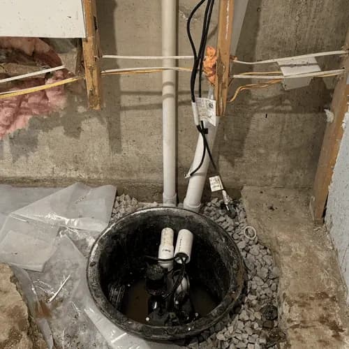 A new sump basin set in gravel in a basement floor with the discharge pipe installed
