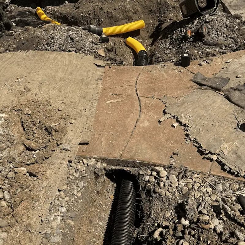 Black drain pipe emerging from a tunnel bored under a concrete walkway