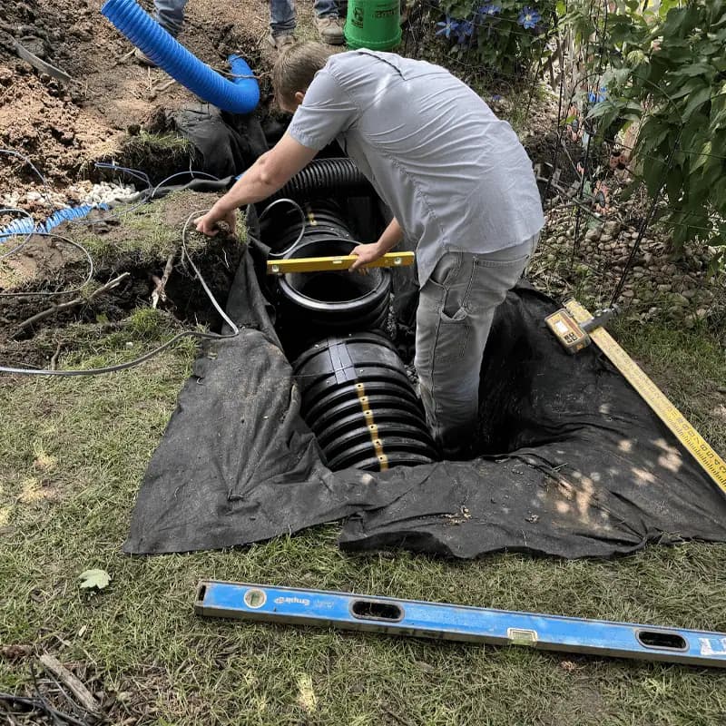 A crew member leveling a tall black outdoor sump basin in a fabric-lined pit in the yard