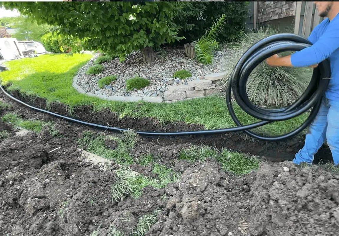 A crew member pulling a long black discharge pipe along a trench across a front lawn