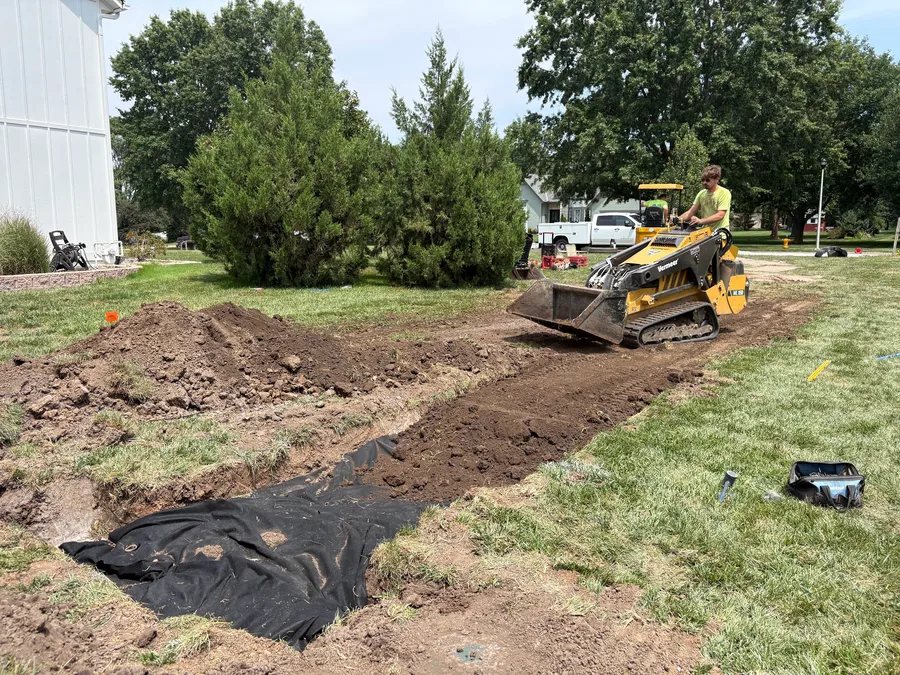 Mini skid steer excavating the trench for a leach bed, fabric already laid in the base